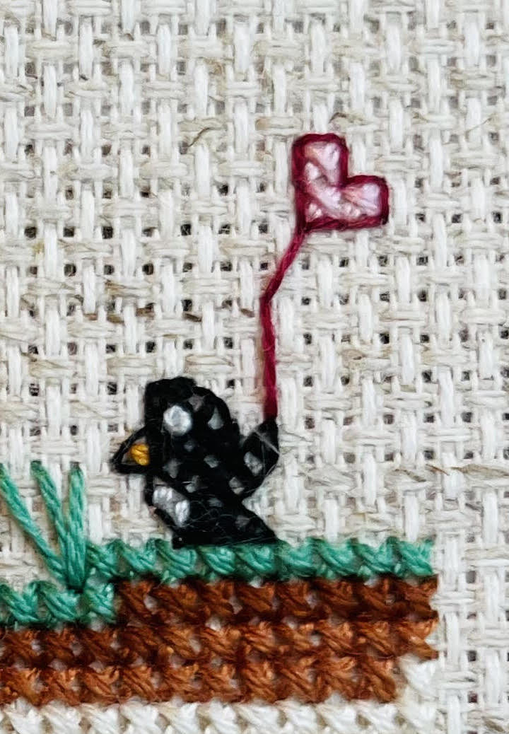 Close up of cross stitch pattern showing a penguin holding a heart shaped balloon